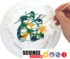Hand holding toothpick swirling different colors of food dye together on top of a plate full of shaving cream